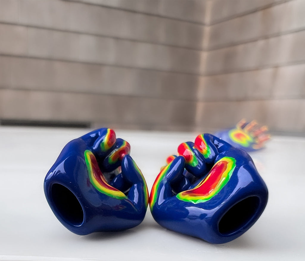 right and left middle finger stud earrings laying down to show that they are hollow. middle finger stud earrings in blue, with the fingers colored in as green, orange, yellow, and red. rainbow colored middle finger earring