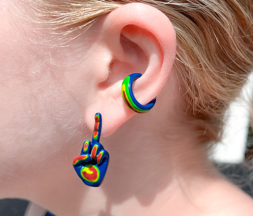 side profile of middle finger stud earring in blue, with the fingers colored in as green, orange, yellow, and red with rainbow ear cuff on ear. rainbow colored middle finger earring