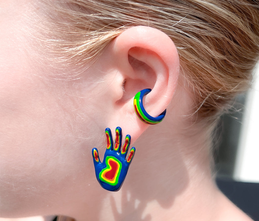 side profile of hand shaped stud earring painted in blue, with the fingers and palm painted in as green, orange, yellow, and red. rainbow colored open hand with fingers earring. hand shaped earring shown on ear along side rainbow ear cuff