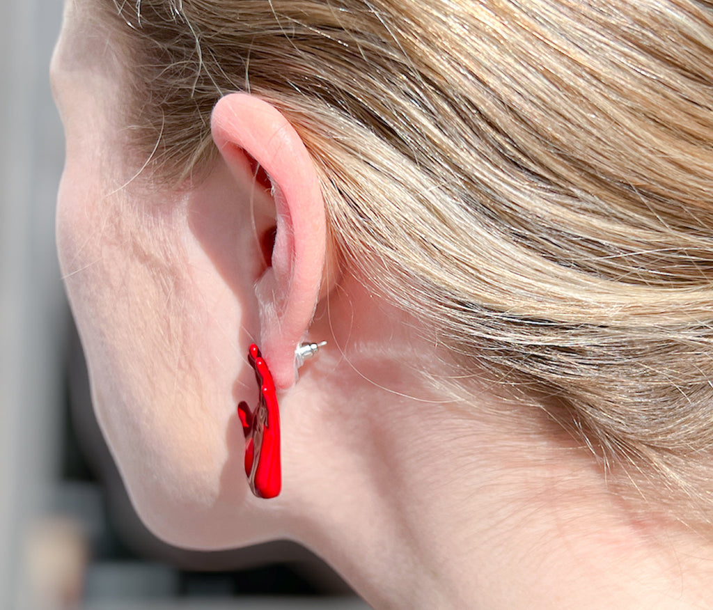 left hand shaped stud earring in red enamel with palm facing outward  on ear
